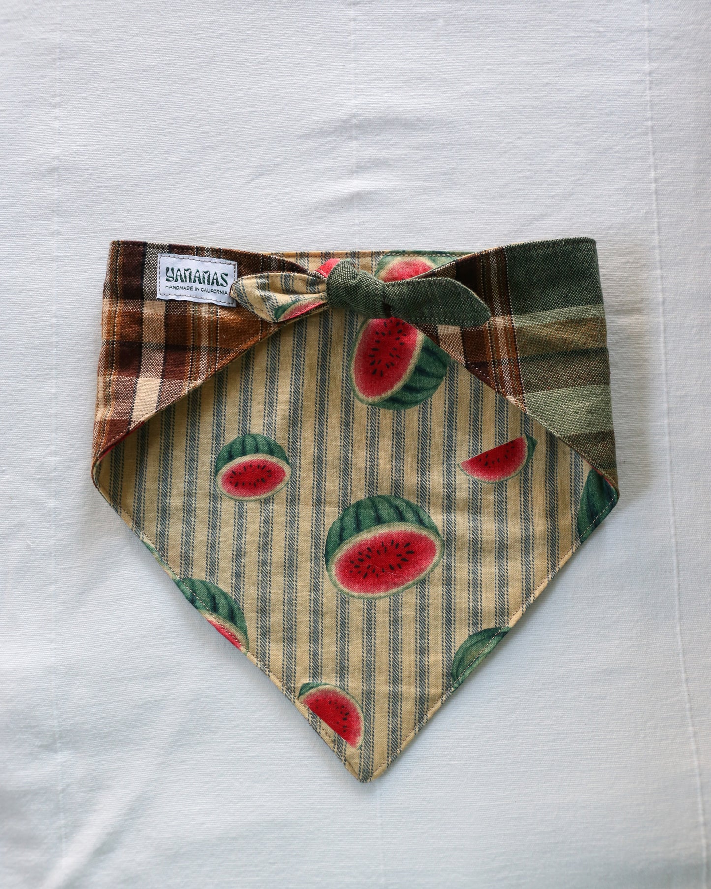 Dog bandana on a plain white background.  Cozy brown-and-green plaid on one side, playful watermelon stripes on the other. Tied as it would be around a pup's neck. 